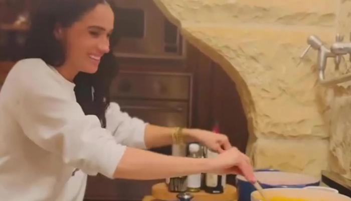 Meghan is seen whipping up something in the kitchen, stirring two pots at once with wooden spoons